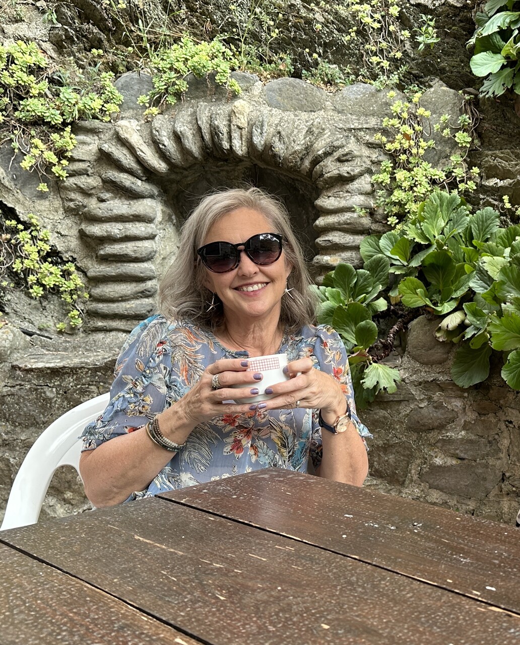 Gina Calvert smiling over a cup of coffee in a garden